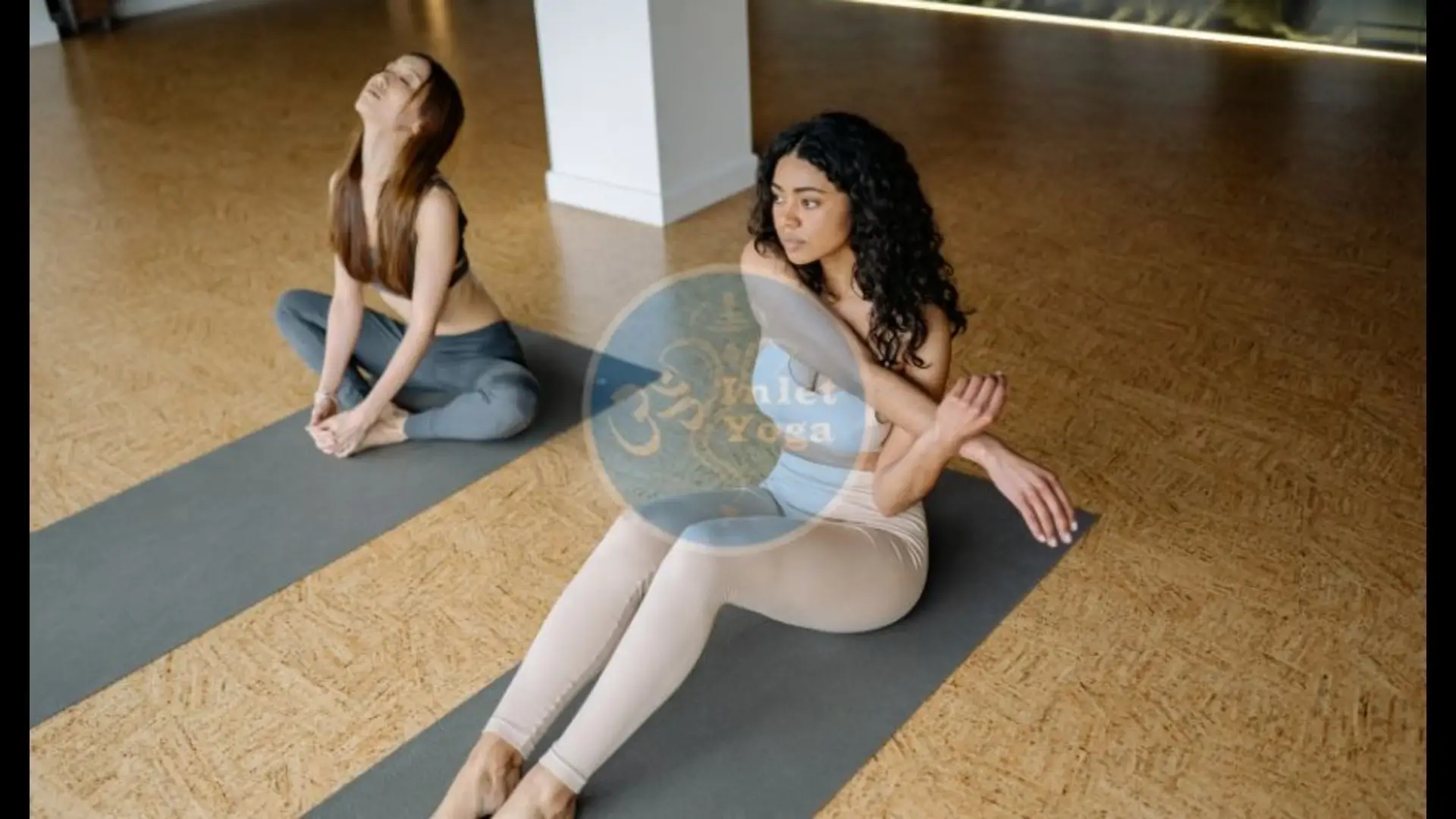 Two women in a private yoga class at Inlet Yoga studio practicing seated poses on cork mats